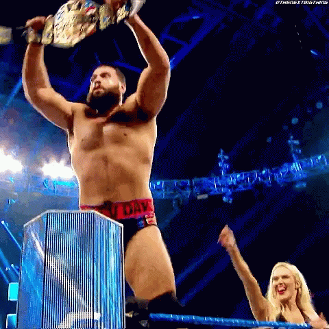 A Wrestler Is Holding A Championship Belt Over His Head While A Woman Watches . GIF