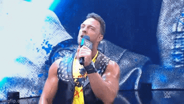 A Wrestler Is Holding A Microphone In His Hand And Talking Into It On A Stage . GIF