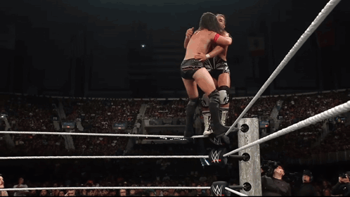 A Wrestler Is Jumping Over A Rope In A Wrestling Ring With A Crowd Watching GIF
