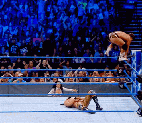 A Wrestler Is Jumping Over Another Wrestler While A Crowd Watches GIF