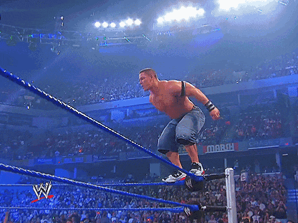 A Wrestler Is Jumping Over The Ropes In Front Of A Crowd With A Sign That Says March GIF