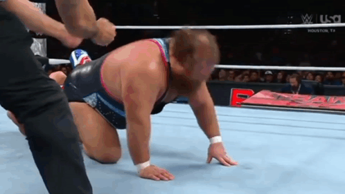 A Wrestler Is Kneeling On The Ground In A Wrestling Ring While A Referee Holds His Hand Over His Head . GIF