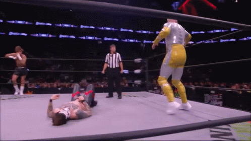 A Wrestler Is Laying On The Ground In A Wrestling Ring While A Referee Watches GIF