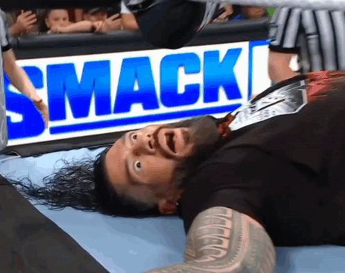 A Wrestler Is Laying On The Ground In Front Of A Smack Sign GIF