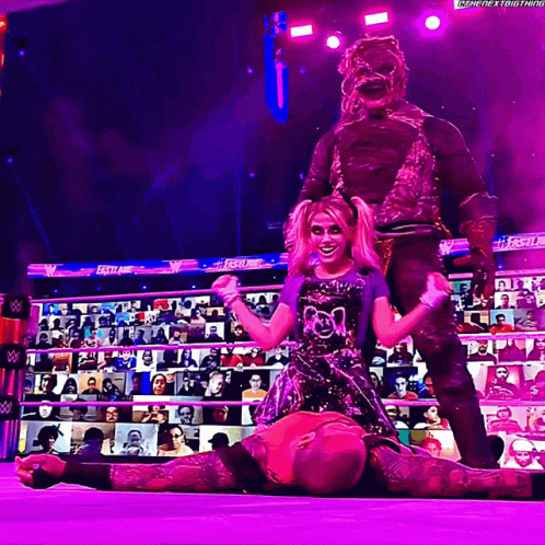 A Wrestler Is Laying On The Ground While A Monster Stands Behind Her In A Purple Ring GIF