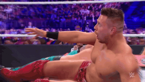 A Wrestler Is Laying On The Ground With His Arm Outstretched In A Wrestling Ring . GIF