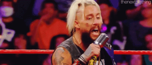 a wrestler is singing into a microphone while standing in a boxing ring .