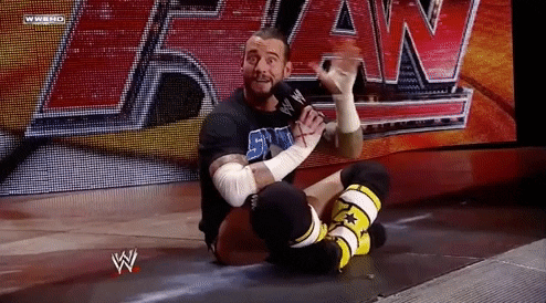 A Wrestler Is Sitting On The Floor With A Microphone In His Hand . GIF