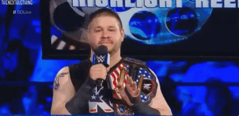 A Wrestler Is Speaking Into A Microphone While Wearing A Wwe Championship Belt . GIF
