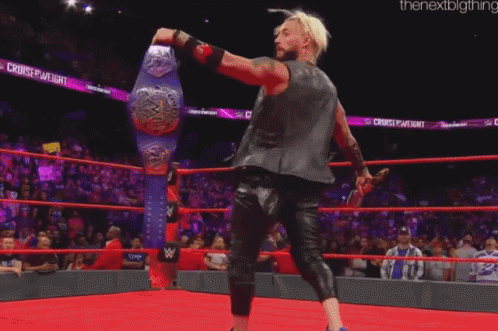 a wrestler is standing in a ring holding a wrestling championship belt