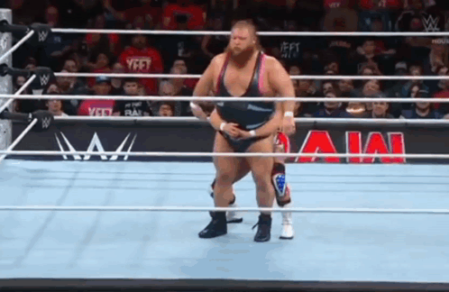 A Wrestler Is Standing In A Wrestling Ring With A Crowd Watching . GIF