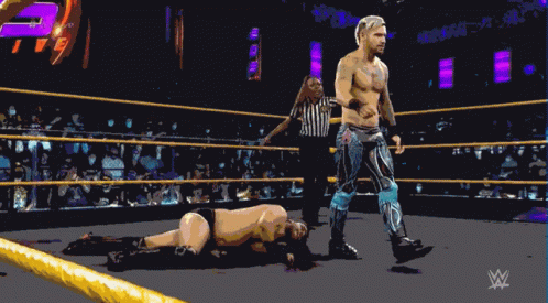 A Wrestler Is Standing In A Wrestling Ring With A Referee GIF