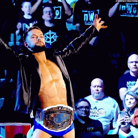 A Wrestler Is Standing In Front Of A Crowd Wearing A World Heavyweight Wrestling Championship Belt . GIF