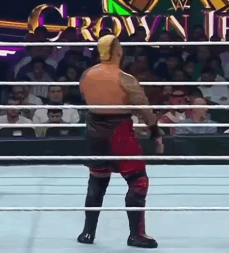 A Wrestler Is Standing In The Middle Of A Wrestling Ring With A Crowd Watching . GIF