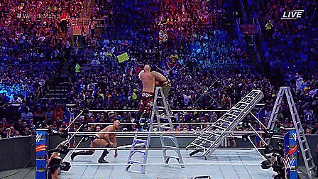 a wrestler is standing on a ladder in a wrestling ring during a match .