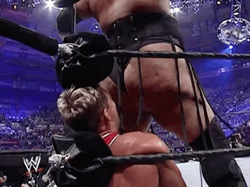 A Wrestler Is Standing On Top Of Another Wrestler In A Boxing Ring . GIF