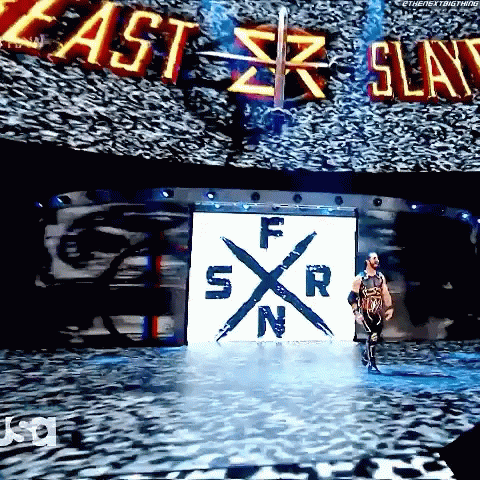 A Wrestler Is Walking Down A Stage With A Large Screen Behind Him That Says East Slay GIF