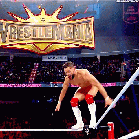 A Wrestler Jumps Over A Rope In Front Of A Wrestlemania Sign GIF