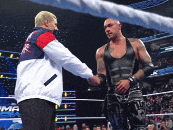A Wrestler Shakes Hands With A Referee In A Ring That Has The Word Emma On It GIF