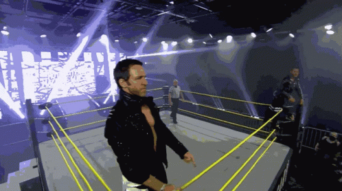 A Wrestler Stands In A Wrestling Ring With A Large Screen Behind Him That Says Wrestling GIF