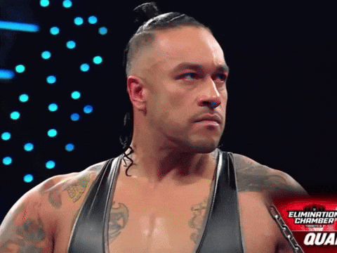 A Wrestler Stands In Front Of A Sign That Says The Elimination Chamber GIF