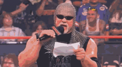 A Wrestler Wearing A Chain Mail Helmet Holds A Piece Of Paper In Front Of A Microphone That Says Wwe GIF