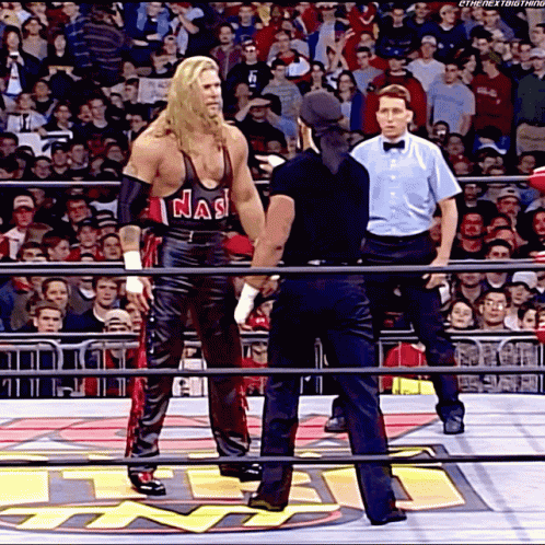 A Wrestler Wearing A Tank Top That Says Nas Is Standing In A Ring With A Referee GIF