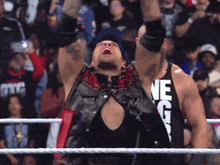 A Wrestler Wearing A Tank Top That Says " Ne G " Holds His Arms In The Air GIF