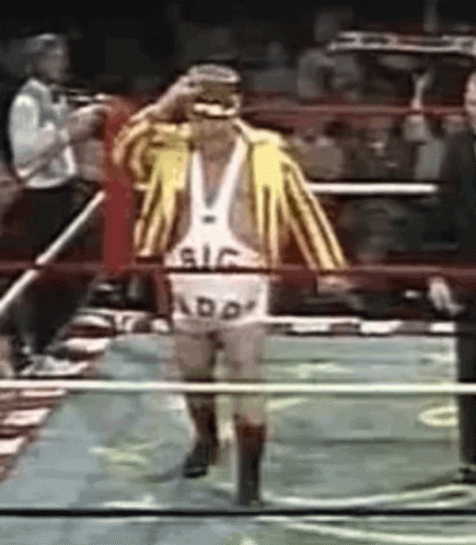 A Wrestler Wearing A Yellow And White Striped Jacket And Shorts With The Word Add On Them Walks Through A Ring GIF