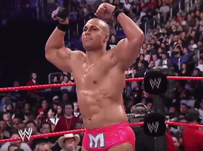 a wrestler wearing pink shorts with the letter m on them stands in a wrestling ring
