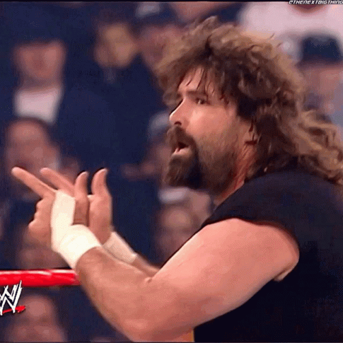 A Wrestler With A Beard And Long Hair Is Pointing His Fingers In The Air GIF