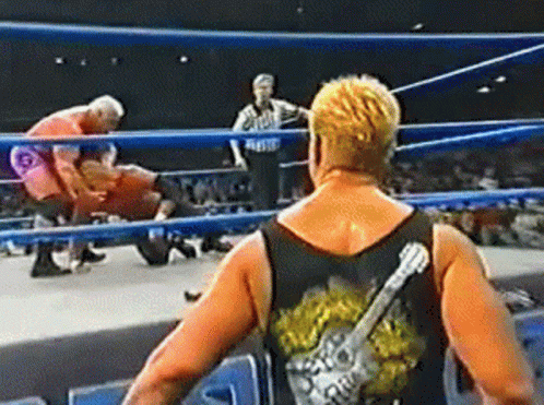A Wrestler With A Guitar On His Back Is Standing In A Wrestling Ring . GIF