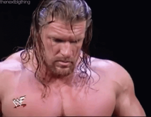 a wrestler with long hair and a beard is standing in a ring without a shirt .