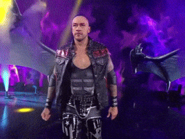 A Wrestler With Wings Is Walking On A Stage In Front Of A Dragon GIF