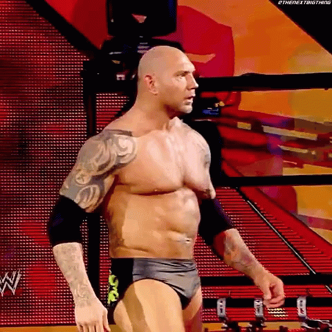 A Wrestler Without A Shirt Is Standing In A Ring With A Red Background . GIF