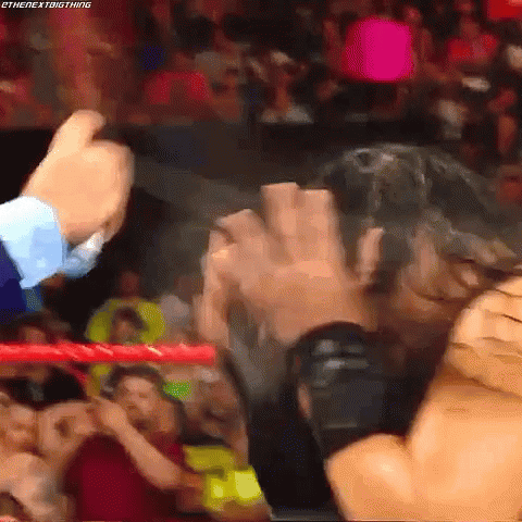 A Wrestling Match Is Going On In A Crowded Stadium And A Man Is Holding Another Man 'S Hand . GIF
