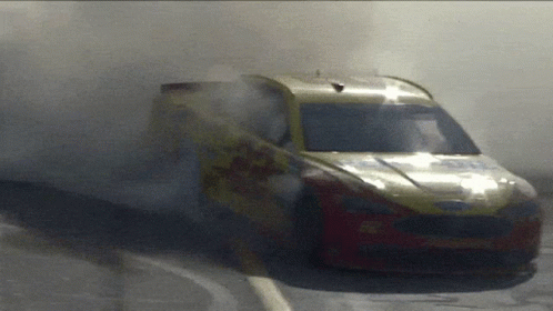 A Yellow And Red Race Car With Smoke Coming Out Of The Windshield GIF