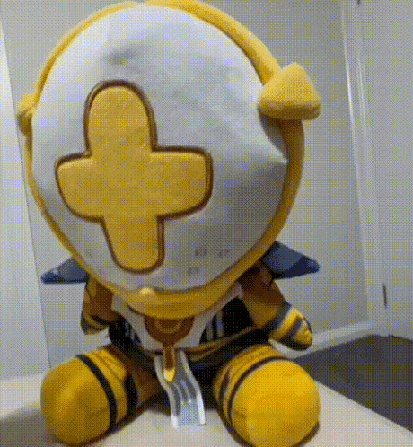 a yellow and white stuffed animal with a yellow cross on its head is sitting on a bed .