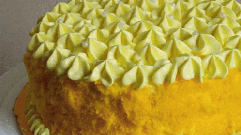 A Yellow Cake With Yellow Frosting And White Pearls GIF