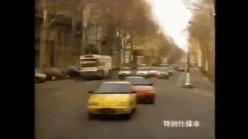 A Yellow Car Is Driving Down A Busy City Street . GIF