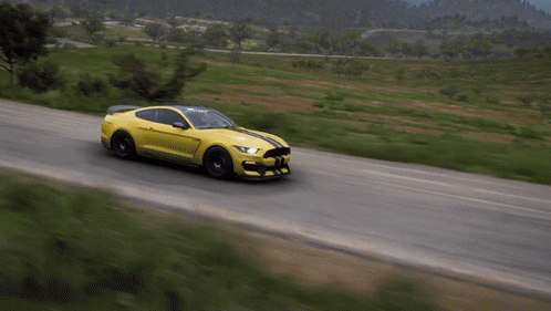 A Yellow Mustang Is Driving Down A Road With Grass On The Side GIF