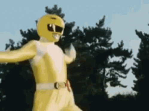 A Yellow Power Ranger Is Standing In Front Of A Forest . GIF