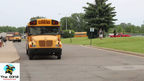 A Yellow School Bus Drives Down A Road GIF