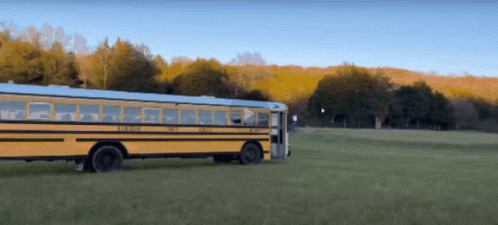 A Yellow School Bus Is Driving Through A Green Field GIF