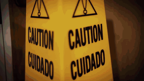 A Yellow Sign That Says Caution And Cuidado GIF