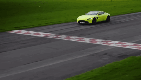 A Yellow Sports Car Is Driving Down A Road With Grass In The Background GIF