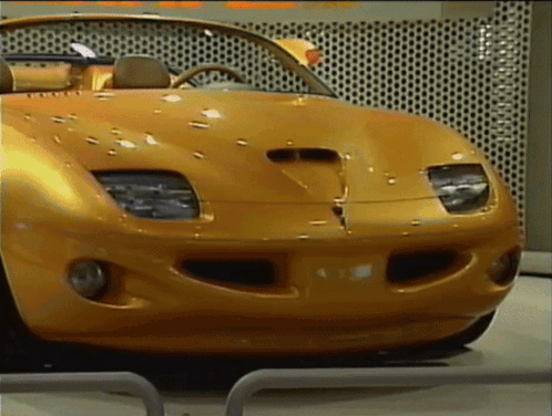 A Yellow Sports Car Is Parked In Front Of A Wall That Has Holes In It GIF