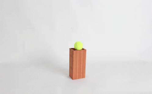 A Yellow Tennis Ball Is Sitting On Top Of A Wooden Block GIF