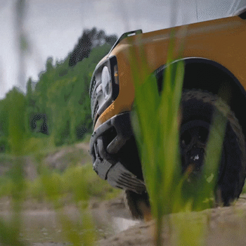 A Yellow Truck Is Driving Through A Grassy Area With Trees In The Background GIF