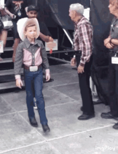A Young Boy Dressed As A Cowboy Is Walking In Front Of A Group Of People . GIF